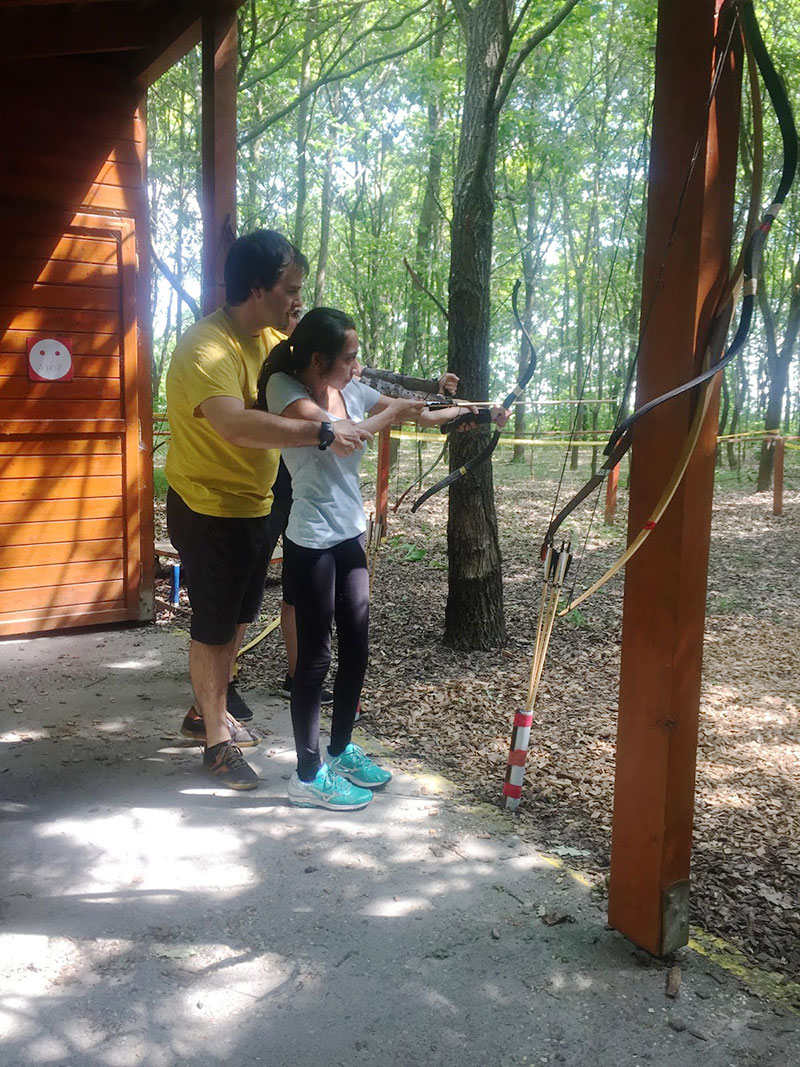 A college student helping a child with a bow and arrow