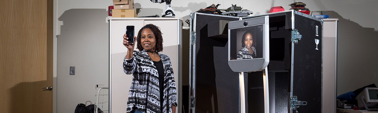 Ayanna Howard looking into a phone that then shows her image on a mobile robot