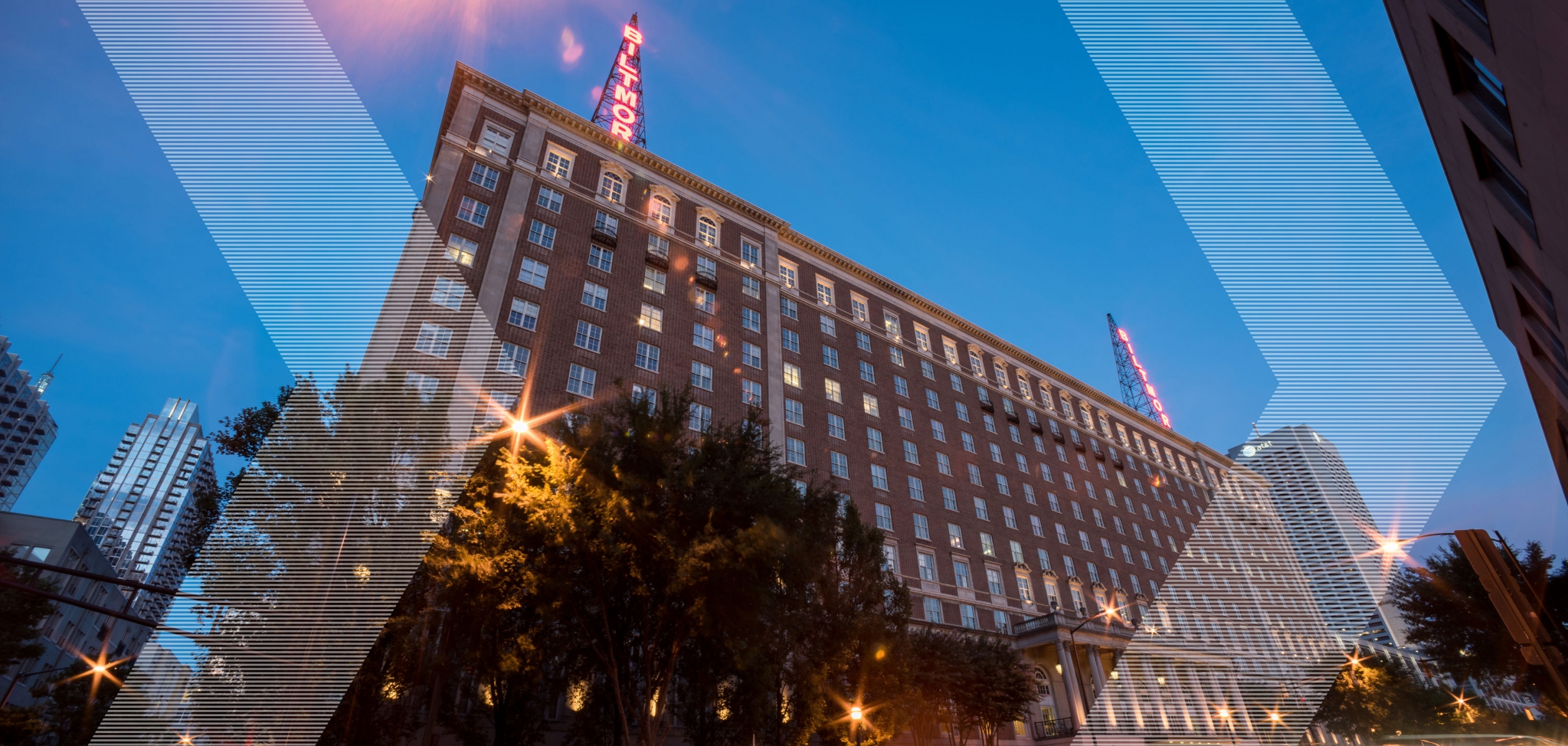 The Biltmore building at night with lighted former radio towers on top that have letters lit up in red that spell out "Biltmore"